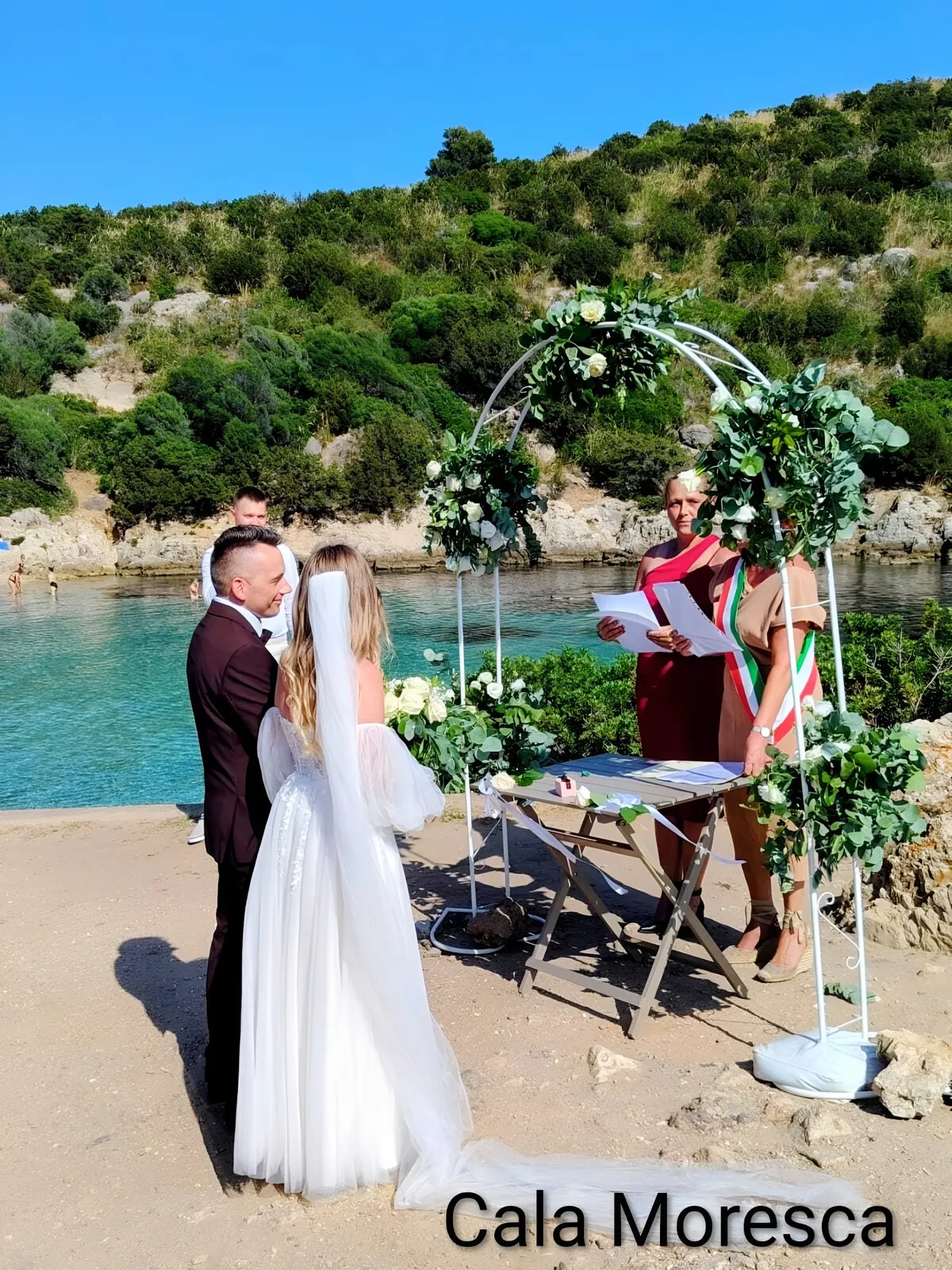 Sposi sotto l'arco di fiori sulla spiaggia di Cala Moresca